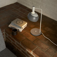 Modern table lamp on a brick surface with books and a mug