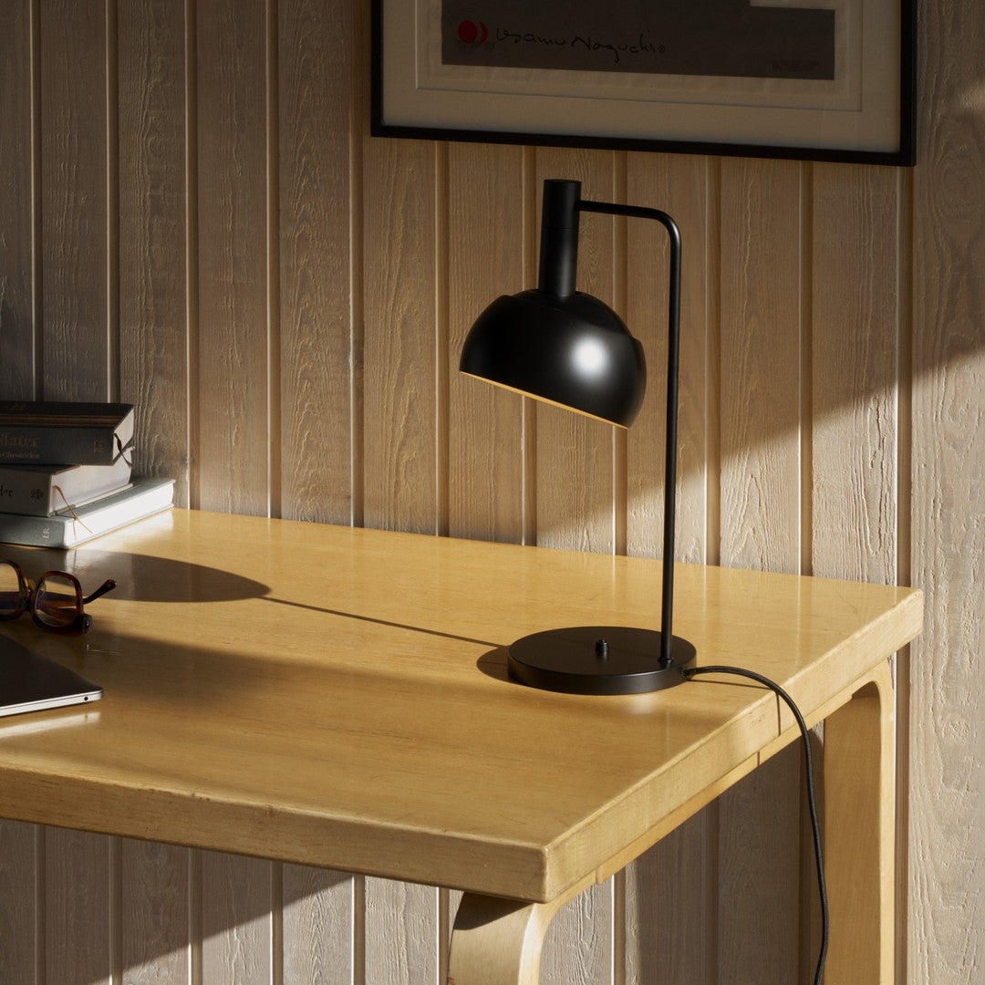 Black lamp on a wooden desk against a wooden paneled wall.