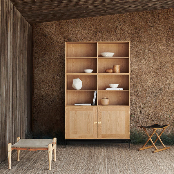 Natural wood bookshelf with light oak finish, smooth surfaces, and minimalist design against a textured earth-toned wall.