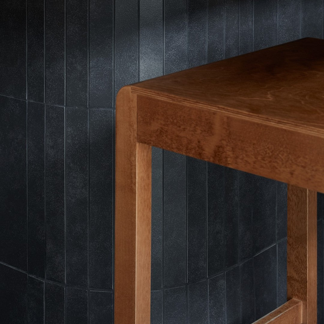 Brown suede table corner against a textured black tile wall, showcasing a modern color contrast and minimalist design.
