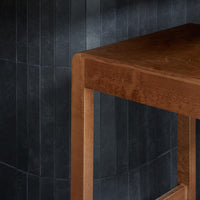 Brown suede table corner against a textured black tile wall, showcasing a modern color contrast and minimalist design.