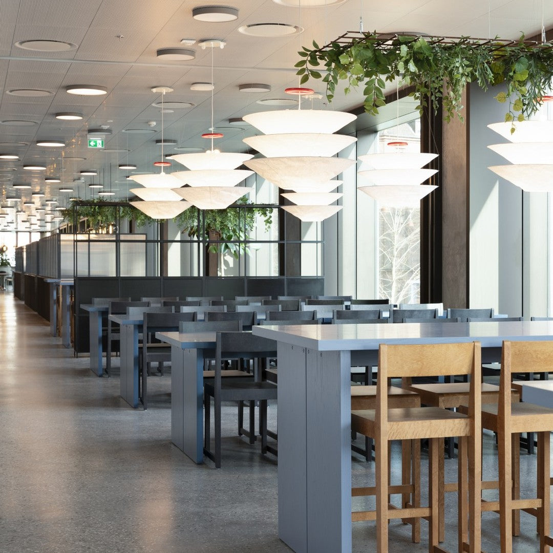 Modern dining space with gray tables, light wood chairs, and unique white pendant lights against a bright, airy backdrop.