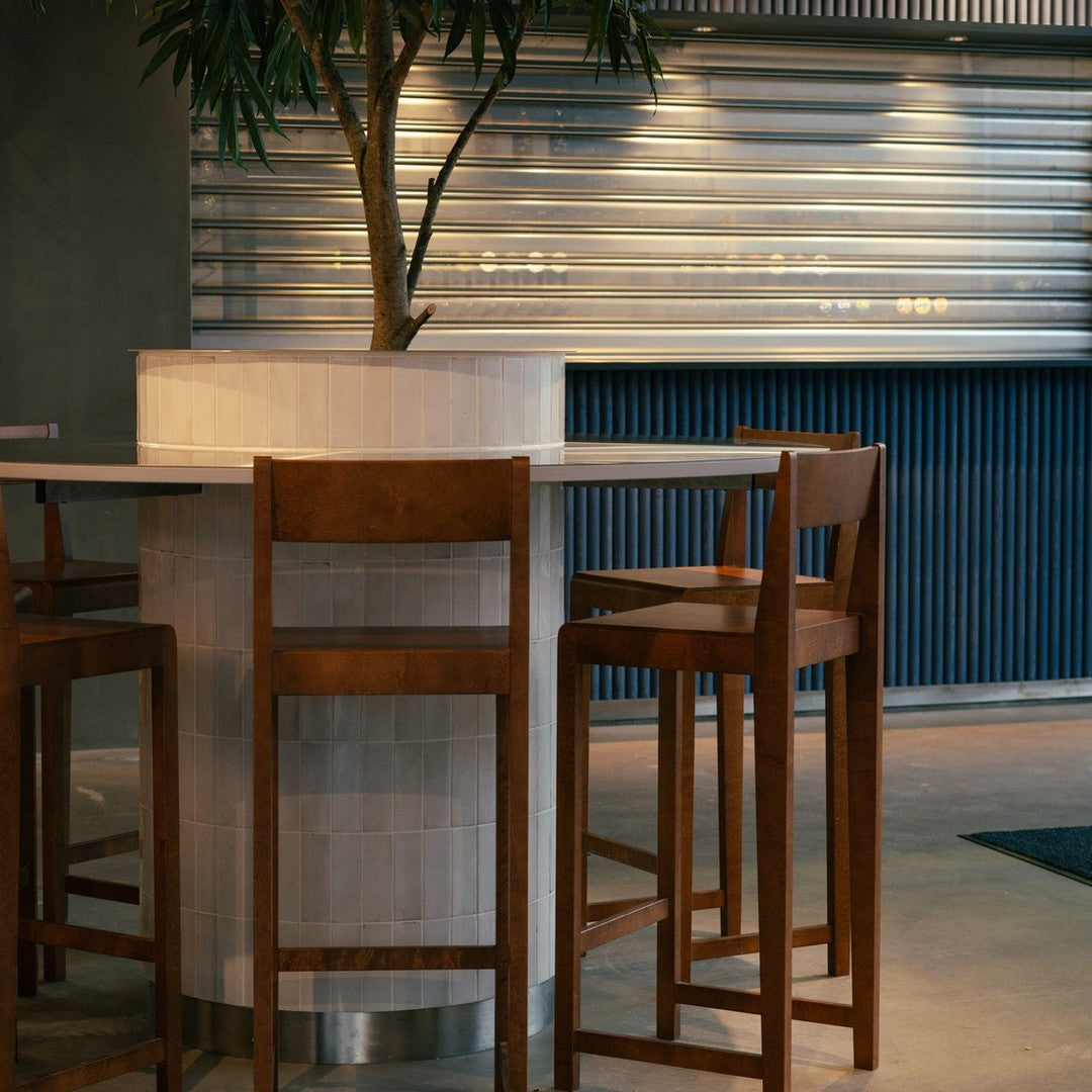 Wooden bar stools with a minimalist design, featuring a mix of light and dark wood tones against a modern gray and blue backdrop.
