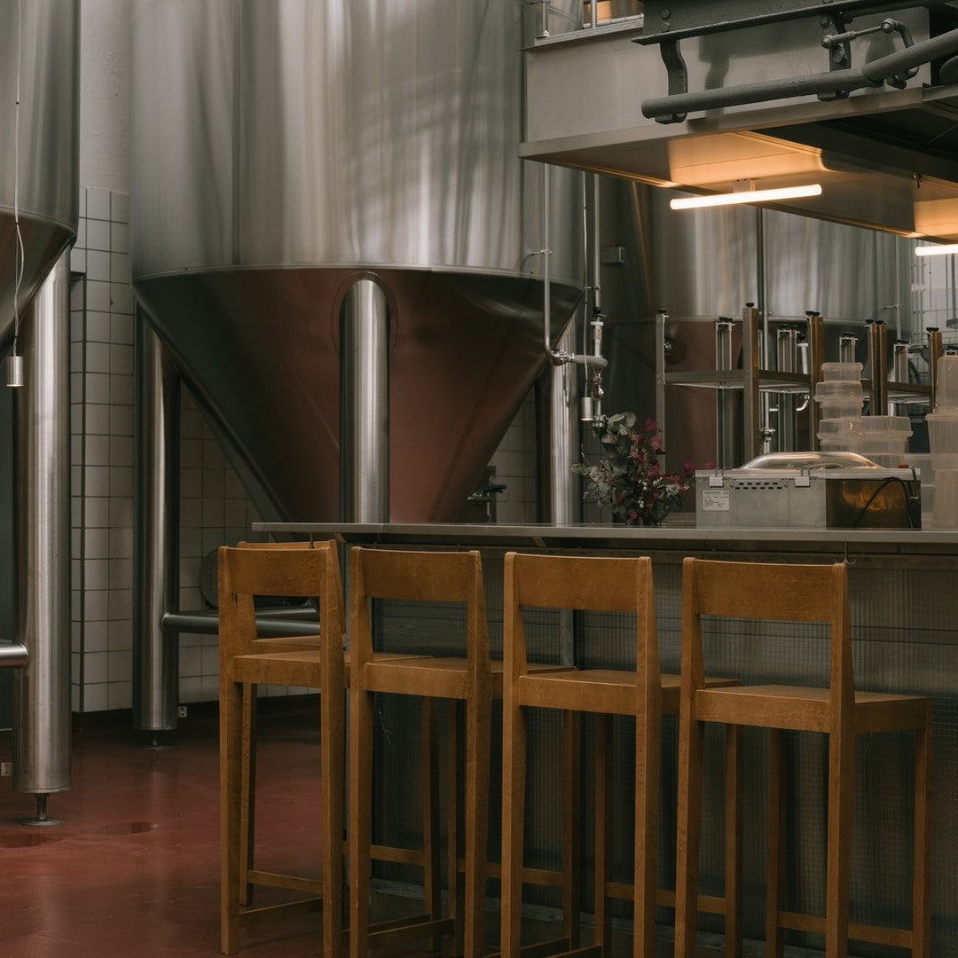 "Modern industrial kitchen with silver brewing tanks and wooden bar stools on a deep red floor."