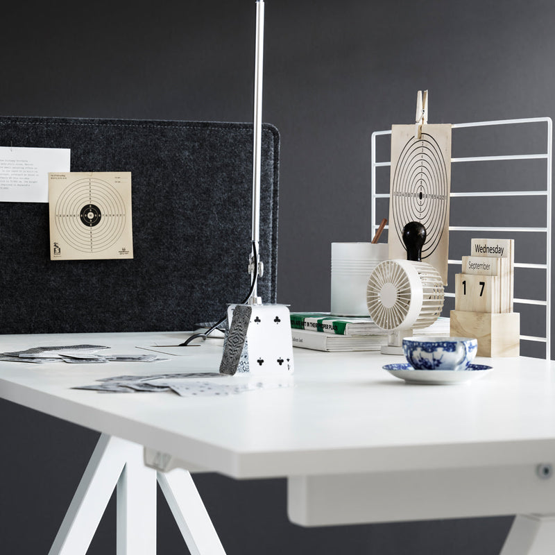 Minimalist desk setup featuring a black felt backdrop, white desk, and geometric patterns in decor elements.