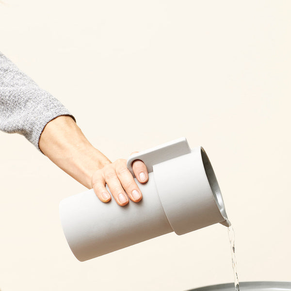 Light gray cylindrical pitcher pouring water, smooth matte finish, minimalistic design, perfect for modern kitchens.