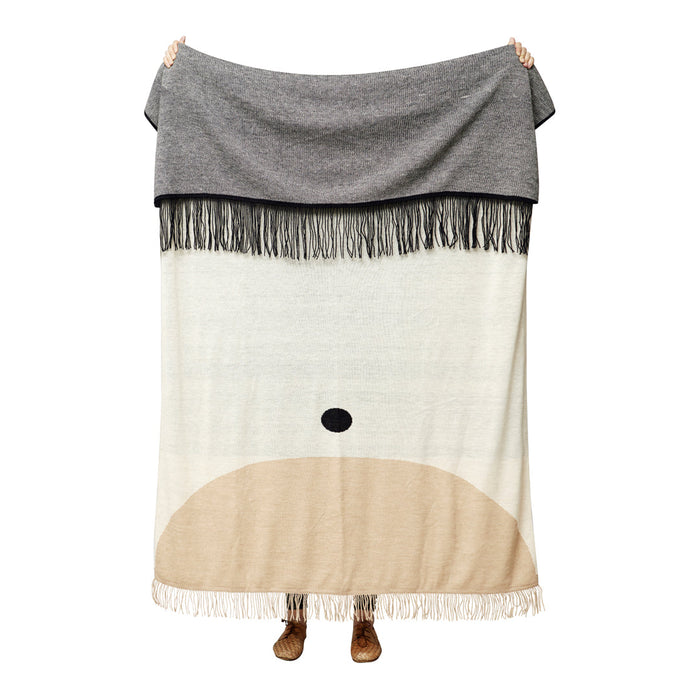 Gray and beige blanket with a whimsical pattern featuring a soft face design and fringe details.