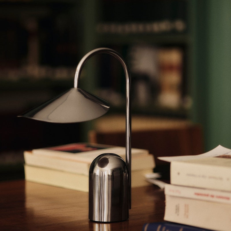 Sleek silver metal desk lamp with a modern design, featuring a curved stem and a geometric shade, on a wooden table.
