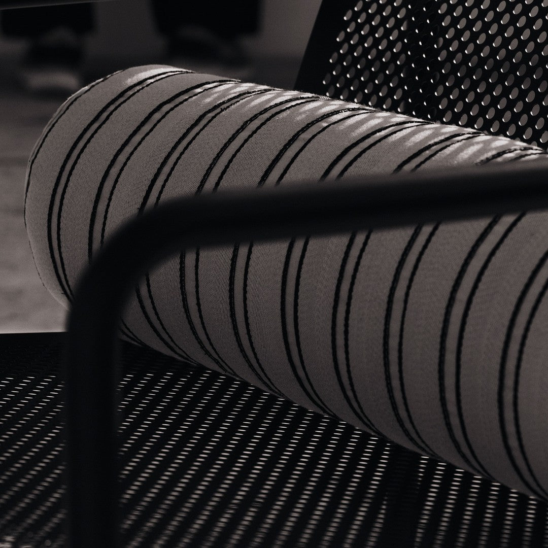 Black and white striped bolster pillow on a textured black chair. Modern, minimalist design for stylish interiors.