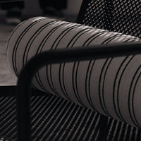 Black and white striped bolster pillow on a textured black chair. Modern, minimalist design for stylish interiors.