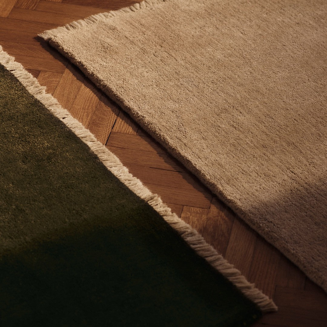 Beige and green textured rugs with fringed edges on a wooden floor. Perfect for modern decor.