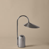 Sleek silver lamp with a curved design and reflective metallic finish, set against a soft beige background.