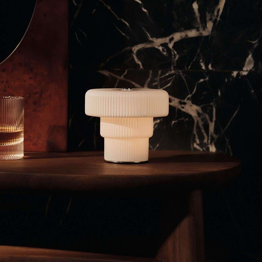 White ribbed lamp on a wooden table, complemented by dark marble and warm glass. Elegant and modern color palette.