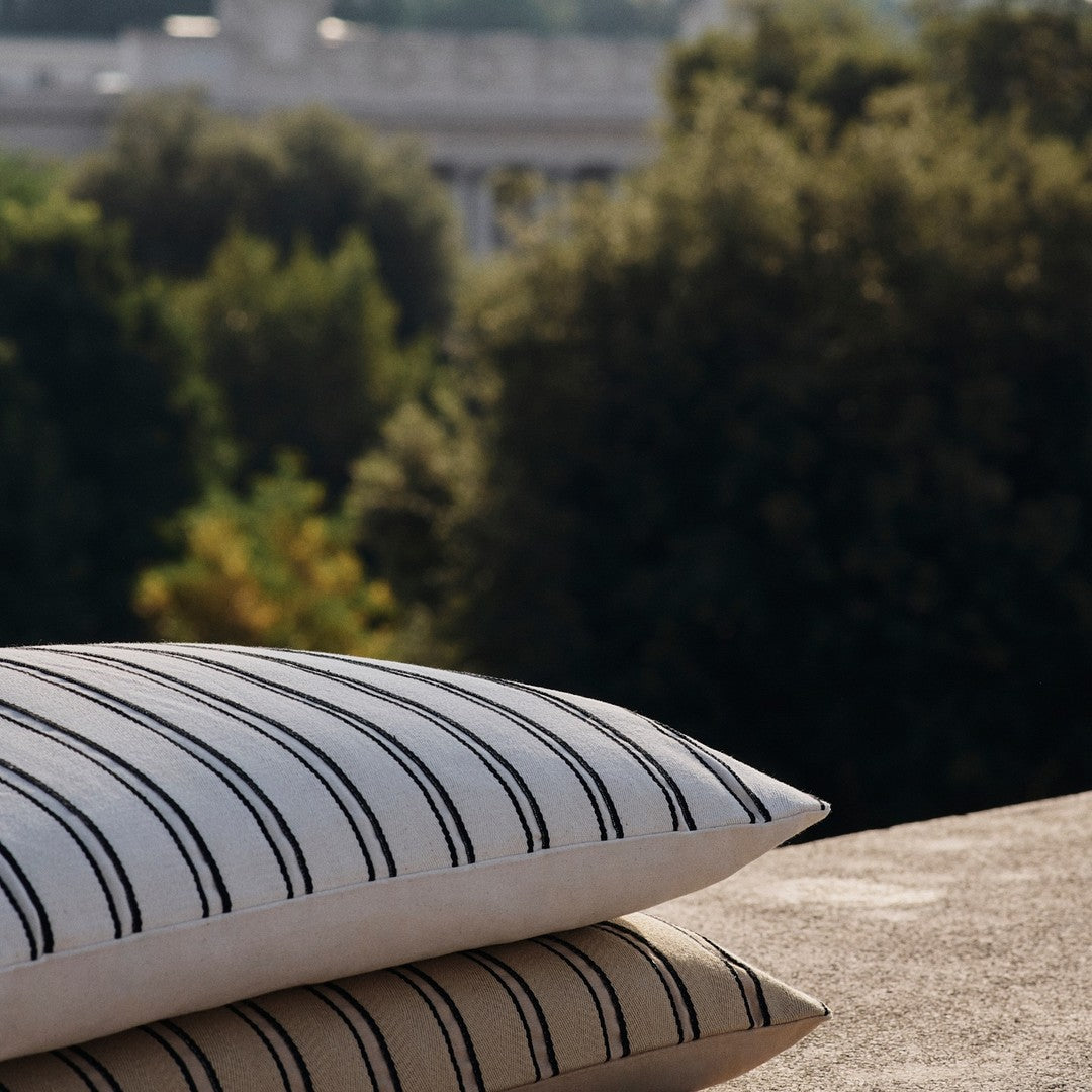White and beige pillows with black stripes, set against a blurred green outdoor background.