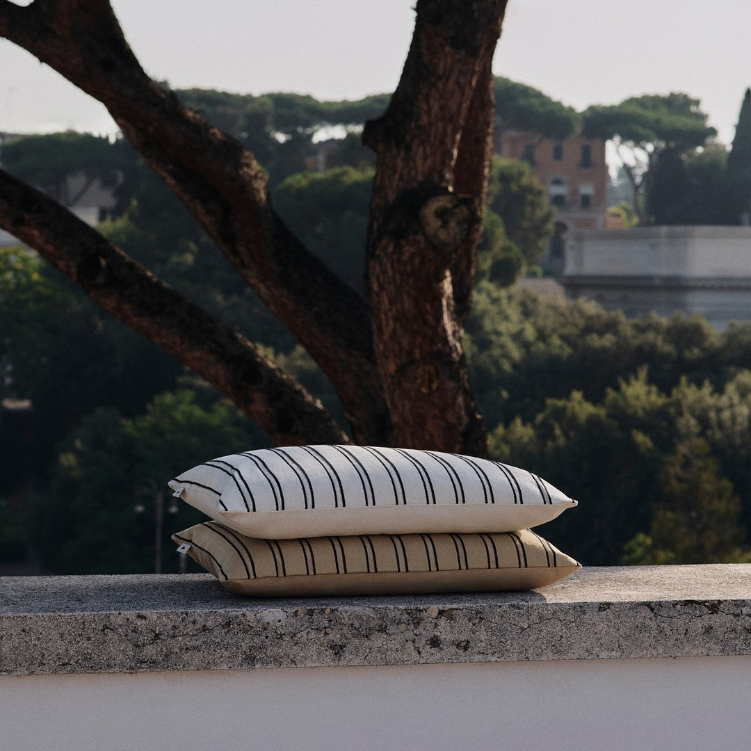 Cream and beige striped decorative pillows stacked outdoors against a natural backdrop.