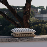 Cream and beige striped decorative pillows stacked outdoors against a natural backdrop.