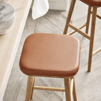 Tan leather cushion on a wooden stool, featuring a smooth texture and minimalist design. Perfect for modern decor.