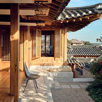 "Modern chair in neutral tones against traditional wooden architecture and blue sky backdrop."