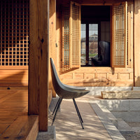 Modern gray chair with sleek black legs, set against a warm wooden interior with lattice patterns and natural light.