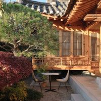 Wooden structure with natural earth tones, vibrant green foliage, and deep red accents in a tranquil outdoor setting.