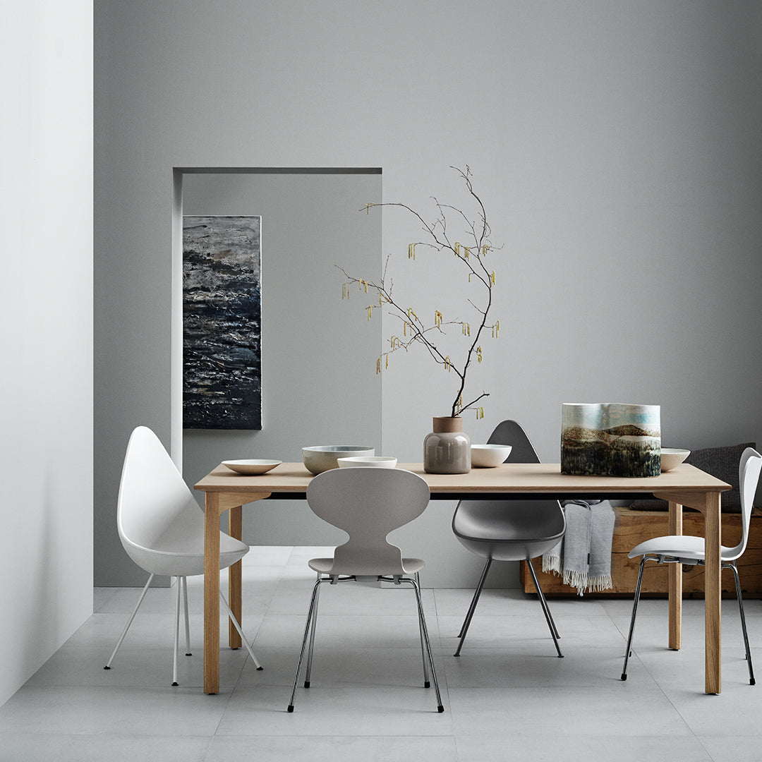 Neutral gray walls with a light wooden table, white and gray chairs, and subtle organic decor accents.