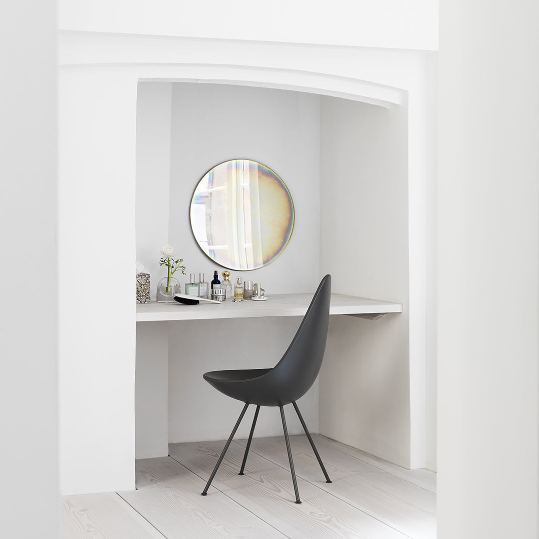 Modern black chair with elegant lines in a minimalist white workspace, featuring a round mirror and subtle natural tones.