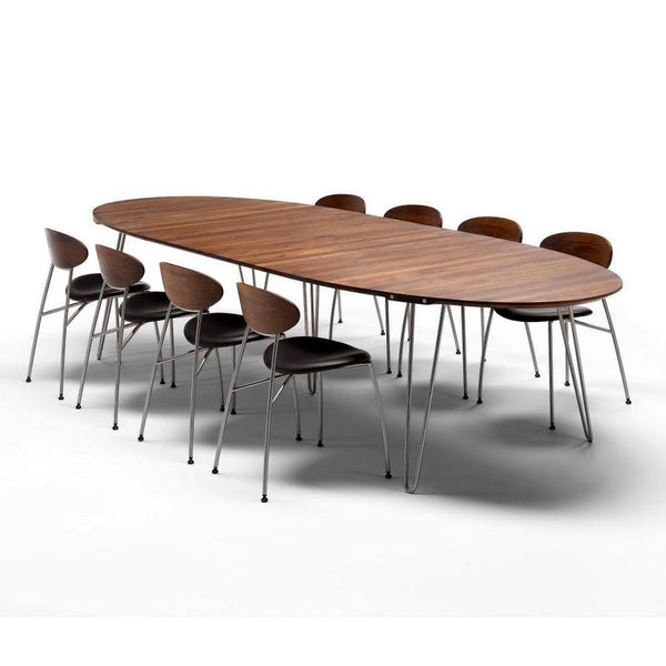 Wooden oval dining table with a rich brown finish and sleek black chairs featuring a modern design and chrome legs.