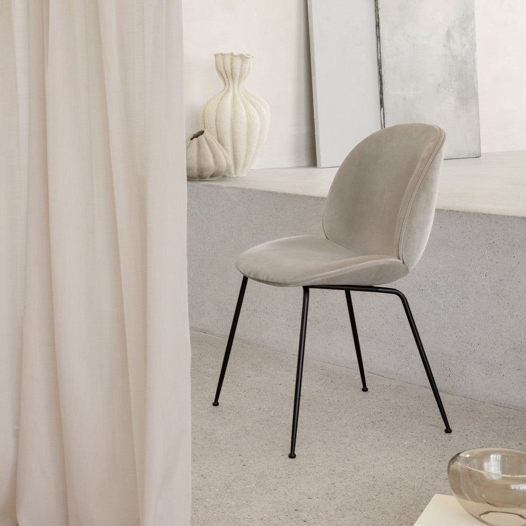 Soft grey velvet chair with a sleek black metal frame, set against light neutral backdrop. Modern and minimalist design.