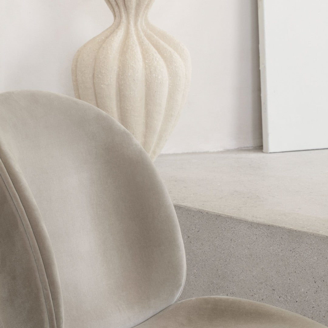 Soft gray velvet chair with smooth curves, paired with a textured cream vase in a minimalist setting.
