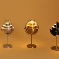 Stylish table lamps in silver, gold, and black with modern circular patterns against a warm orange background.