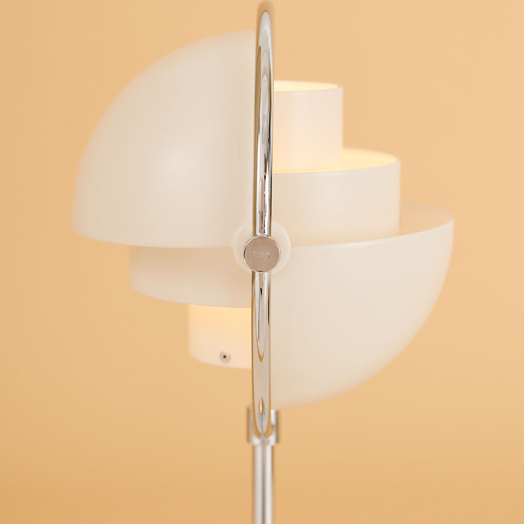 White modern lamp with circular layered shades, featuring a sleek silver base against a warm beige background.