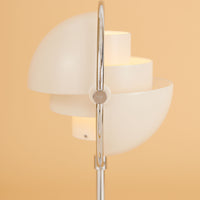 White modern lamp with circular layered shades, featuring a sleek silver base against a warm beige background.