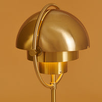 Brass lamp with a sleek, dome-shaped shade and elegant curved details against a warm orange background.