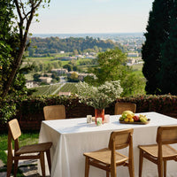 "Bright white tablecloth on a wooden table, with greenery and colorful fruits for an elegant outdoor dining setup."