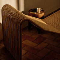 Natural woven fabric in warm beige tones, featuring a sleek, curved design on a rustic tiled floor.