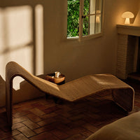 Elegant woven lounge chair in natural beige tones, featuring smooth curves and a textured pattern against a warm, sunlit backdrop.