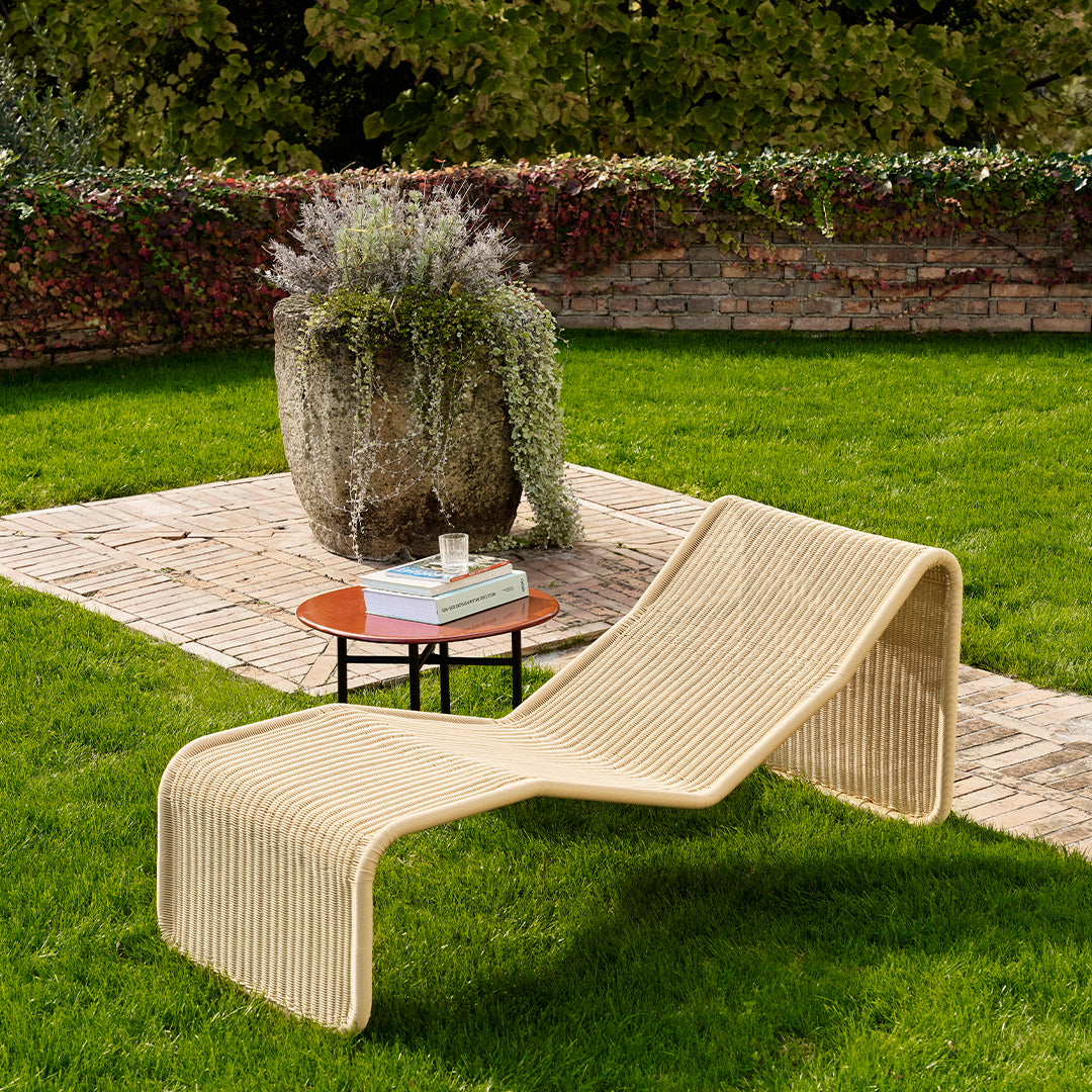 Beige woven lounge chair with a smooth, modern design, set against lush green grass and rustic stone pathway.