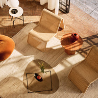 Natural beige wicker chairs on a textured light rug, paired with a round wooden side table and warm orange decor.