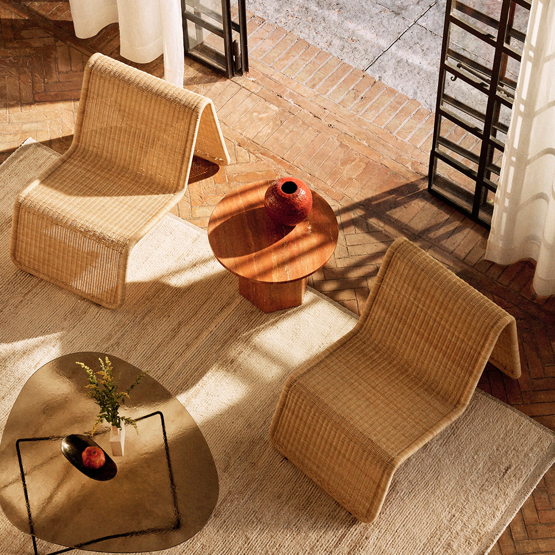 Woven rattan lounge chairs in beige, paired with a wooden table on a light textured rug, creating a warm, inviting space.