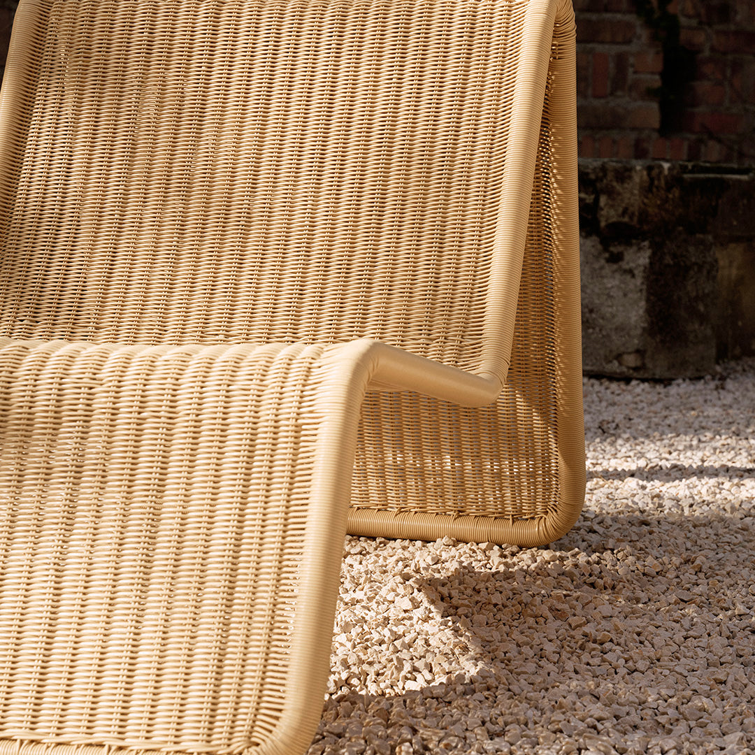 Beige woven lounge chair with vertical ribbed pattern, set against white pebbles. Perfect for outdoor decor.