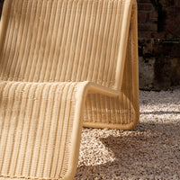 Beige woven lounge chair with vertical ribbed pattern, set against white pebbles. Perfect for outdoor decor.