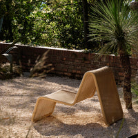 Sleek tan lounge chair with a modern wavy design, set against a lush green garden backdrop.