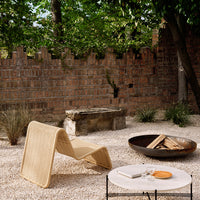 Natural woven lounge chair in beige, surrounded by a neutral gravel setting and rustic brick wall accents.