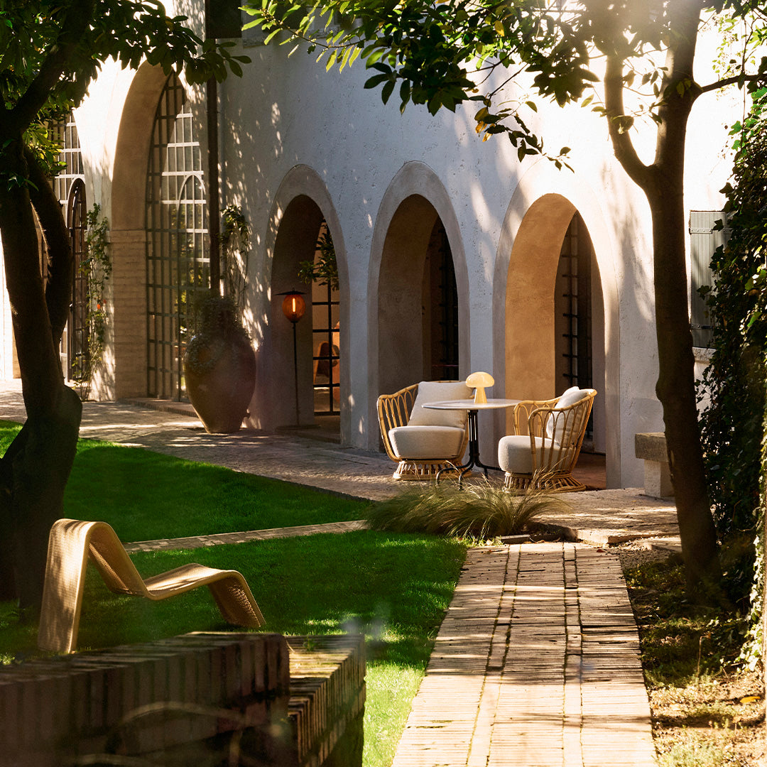 Chic outdoor space featuring neutral-toned furniture, arched architecture, and lush green grass under warm sunlight.