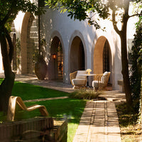 Chic outdoor space featuring neutral-toned furniture, arched architecture, and lush green grass under warm sunlight.
