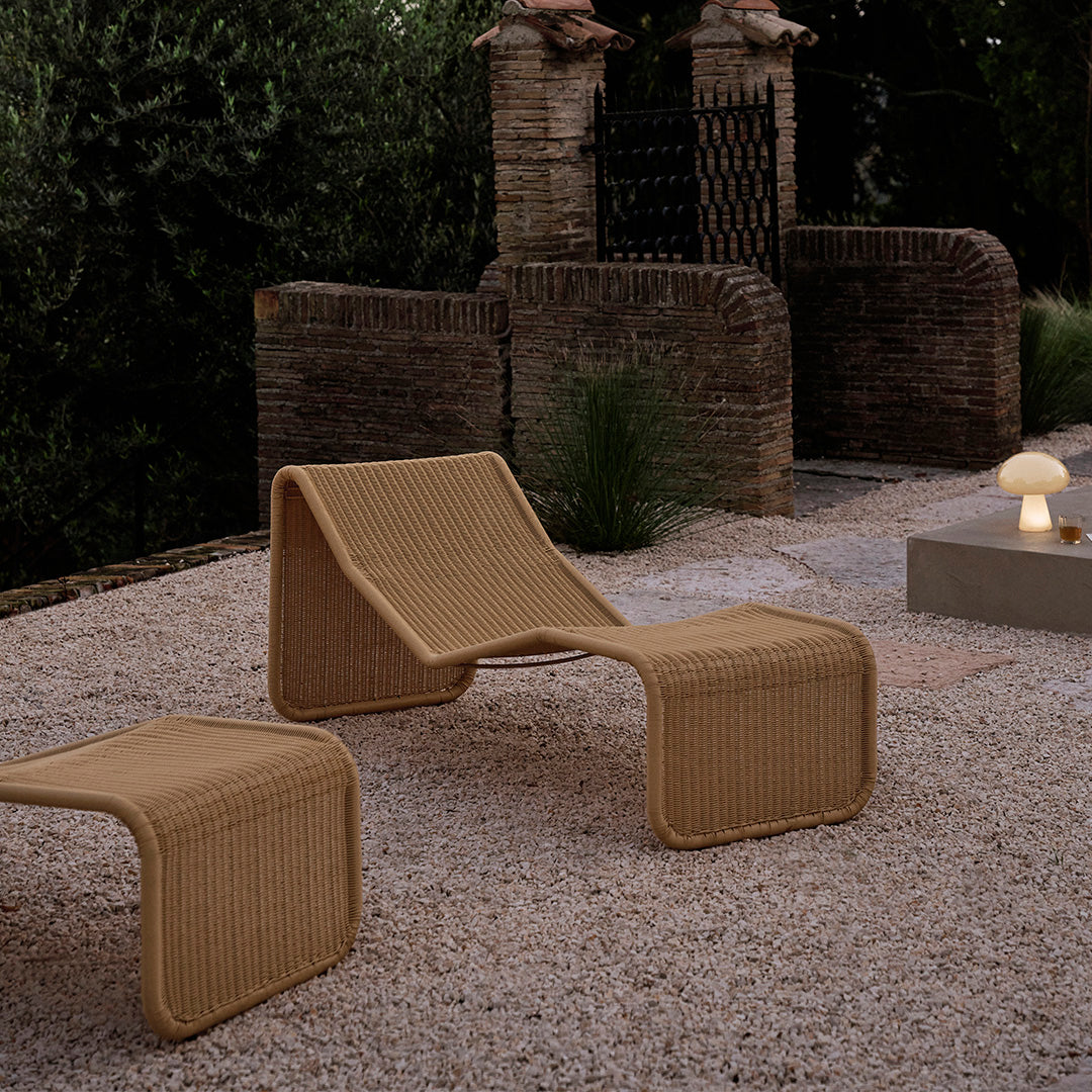 "Beige outdoor lounge chairs with a textured pattern, set against a rustic stone backdrop in a tranquil garden."