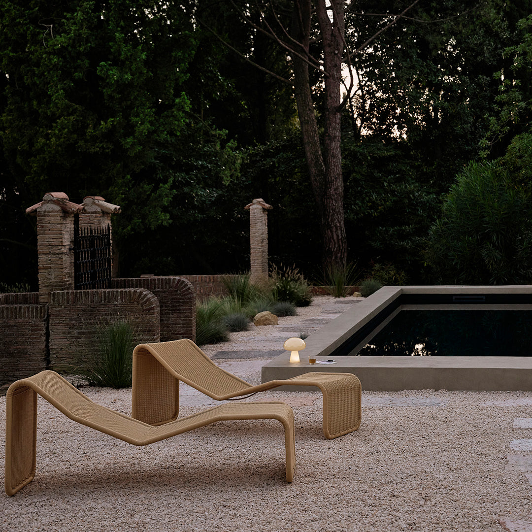 Textured beige lounge chair against a dark pool, surrounded by greenery and soft earth-toned gravel.