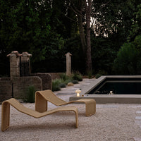 Textured beige lounge chair against a dark pool, surrounded by greenery and soft earth-toned gravel.