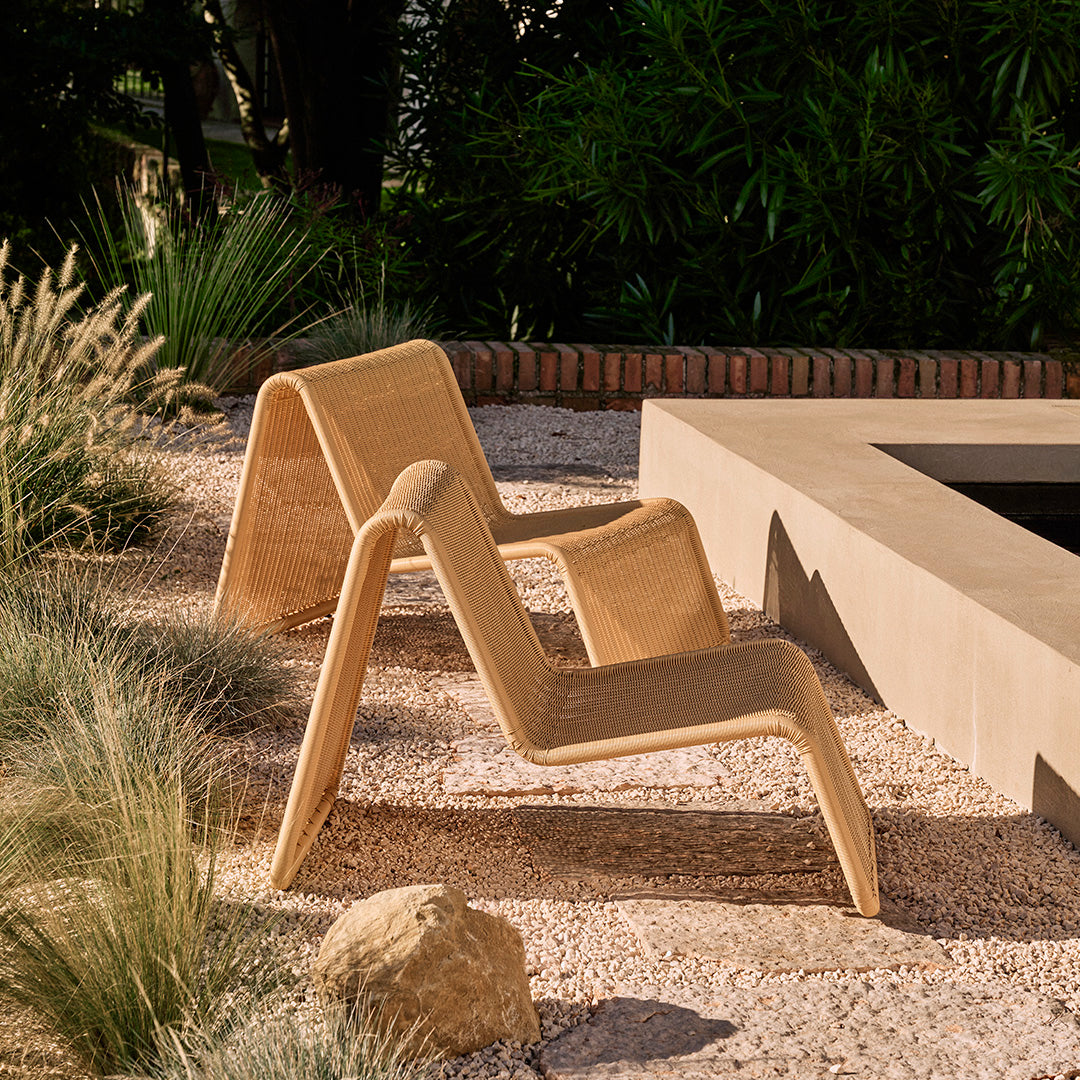 Beige lounge chair with a modern, minimalist design, set against a natural outdoor backdrop.