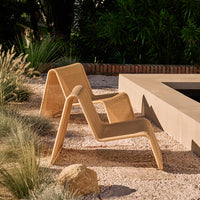 Beige lounge chair with a modern, minimalist design, set against a natural outdoor backdrop.